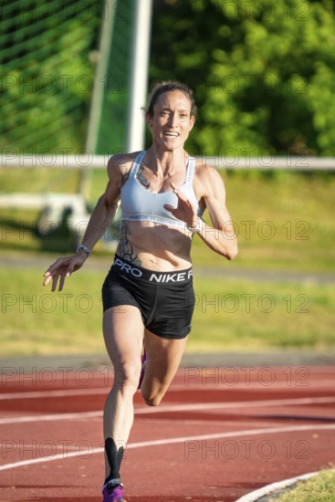 Woman running with energy on a sports track in green surroundings, middle distance runner Katharina