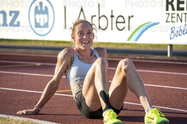 Sportswoman sits exhausted but satisfied on the track, smiling and relaxing, middle distance runner