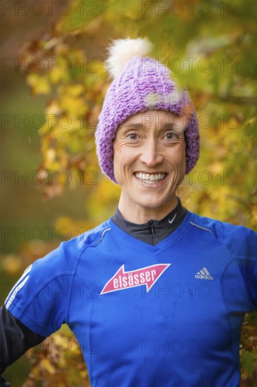 Woman wearing purple hat and blue sweater smiling in autumn surroundings, middle distance runner