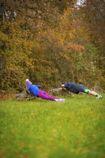 Two people doing push-ups on rocks in an autumnal forest, middle distance runner Katharina Jaiser,