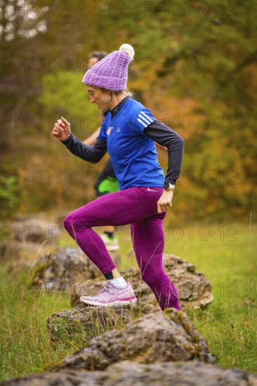 Woman in sporty clothing climbs energetically on rocks in autumn nature, middle distance runner