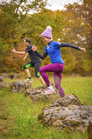 Two people jumping during dynamic training on rocks in autumn forest, middle distance runner