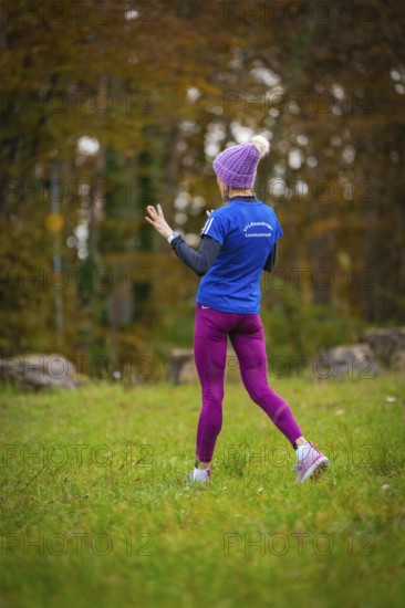Woman in sporty clothes running in the forest surrounded by autumn trees, middle distance runner
