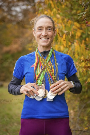 Woman proudly showing her medals in an autumnal setting, middle distance runner Katharina Jaiser,