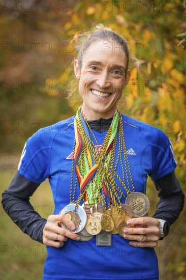 Woman with many medals around her neck smiling in autumn scenery, middle distance runner Katharina