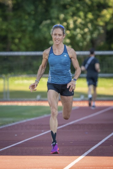 Athlete runs purposefully on the track in green, sunny surroundings, middle distance runner