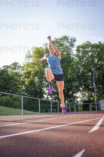 Athlete jumping on a track surrounded by green trees and bright sunshine, middle distance runner