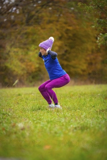 Woman wearing colorful sportswear doing jumping exercises on an autumnal meadow, middle distance