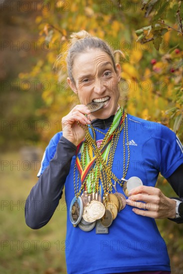 Woman with medals playfully bites on a medal and smiles, middle distance runner Katharina Jaiser,