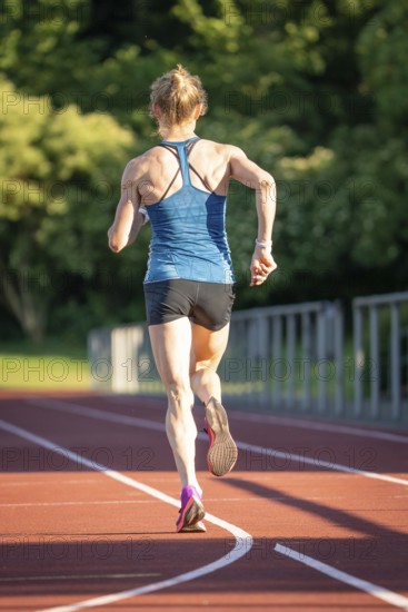 Back view of a running athlete on a red track surrounded by nature, middle distance runner