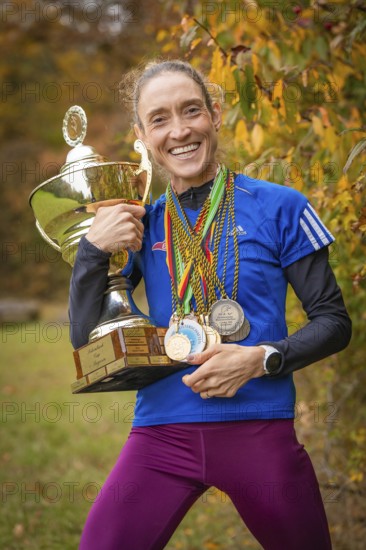 Happy woman holding trophy and medals in autumn surroundings, middle distance runner Katharina