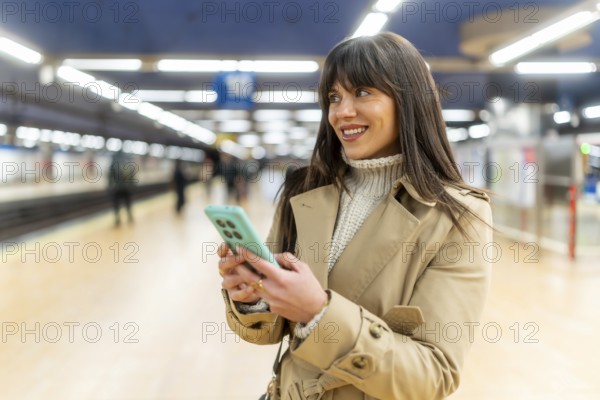Woman standing on a train station platform, smiling and looking away while sending messages or
