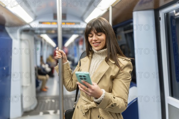 Young woman standing in a subway car, smiling at her smartphone screen during the commute, browsing