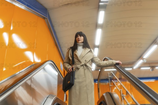 Woman travelling on an escalator in a subway station, holding onto the handrail, dressed in a