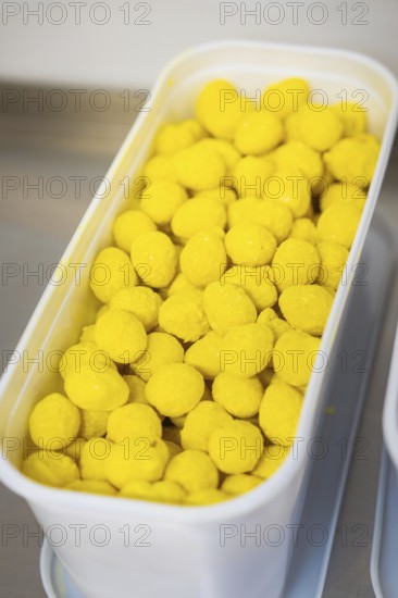 Many yellow balls in a plastic container, presented industrially, chocolate quail eggs, Easter