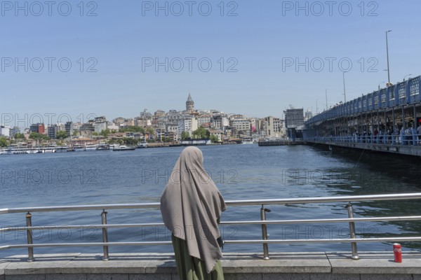 Istanbul, Turkey. June 23rd 2025. A Muslim women looks out across the Golden Horn towards the