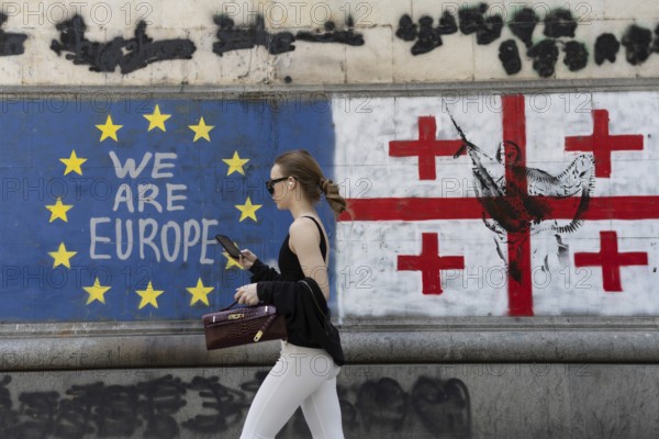 Tbilisi, Georgia. July 7th 2025. A woman walks past the flags of Georgia and the European Union