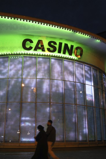 Tbilisi, Georgia. September 4th 2025. A tourist couple walk past an illuminated window for a casino