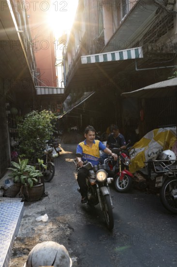 Bangkok, Thailand. March 18th 2025. A motorcycle mechanic rides through the narrow streets of Talat