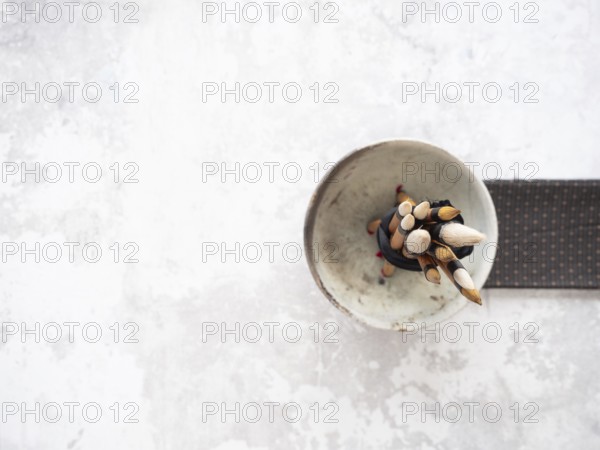 Paint brushes with bamboo handles are bundled together in a ceramic bowl, resting on a white table