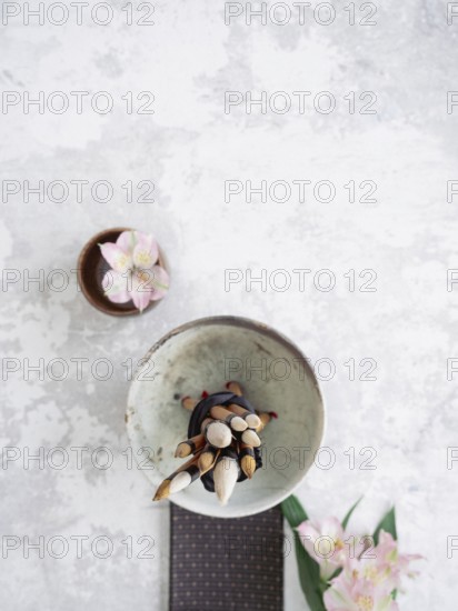 Calligraphy brushes tied together in a bowl on a textured background with pink flowers and a