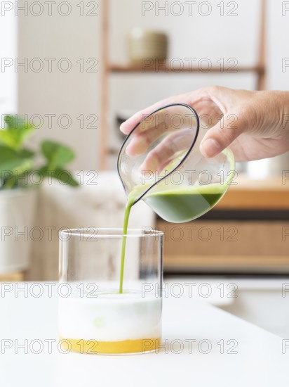 Hand pouring vibrant green matcha into a glass of mango base and milk, creating a layered drink
