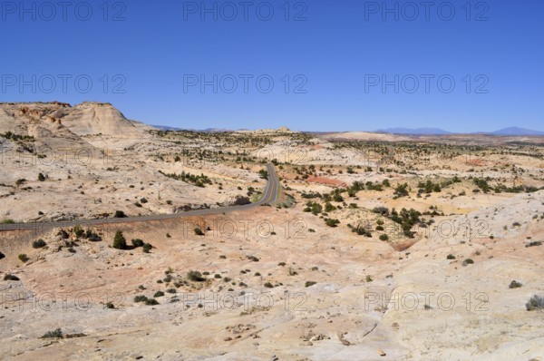 Paved road winds through dry landscape with reddish hills and sparse vegetation, Grand Staircase