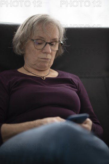 Elderly woman with glasses, gray hair, sitting on sofa and using smartphone, cell phone, Stuttgart,