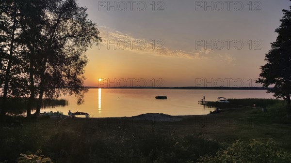 A quiet, atmospheric sunset on a lake with trees and a boat dock, bicycle tour through Masuria,