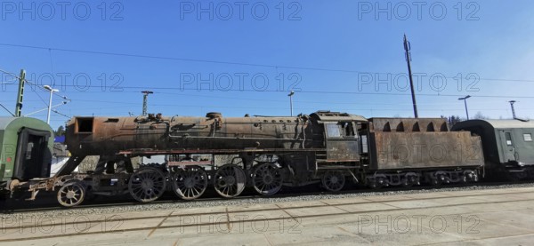 Transfer of a rusted historic steam locomotive on rails under clear blue skies at the train