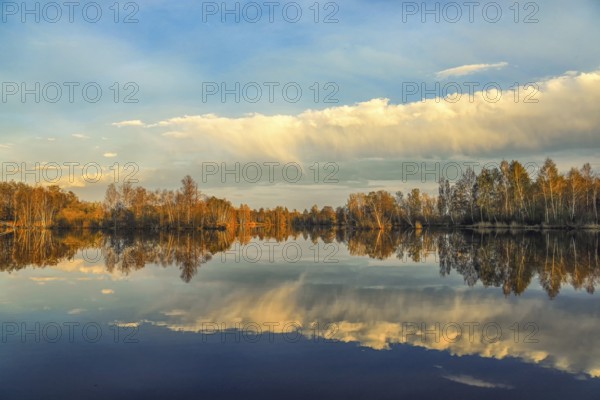Tranquil landscape with autumn trees reflecting in the still lake, surrounded by a blue sky with