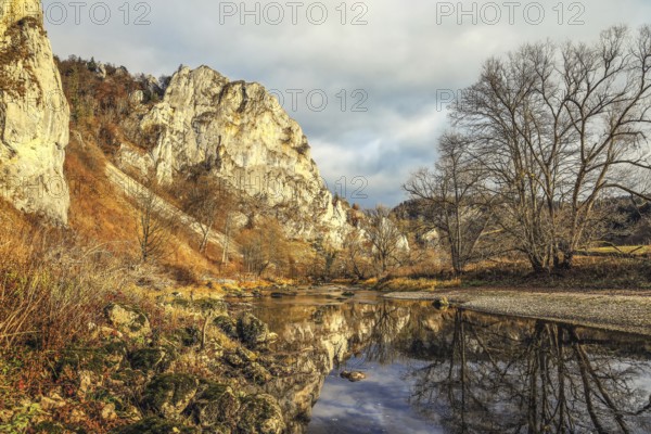 An autumn landscape with a river reflecting the surrounding rocks and trees, under a cloudy sky,