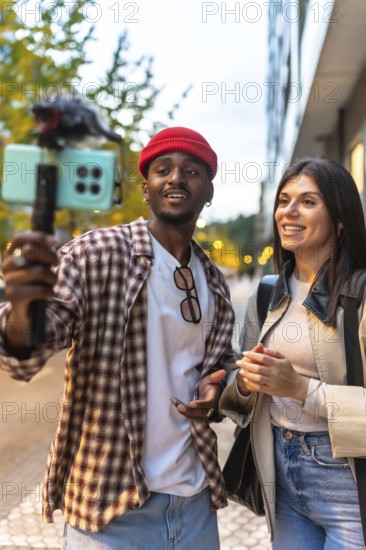Diverse couple vlogging outdoor, enthusiastically recording video on a smartphone with a microphone