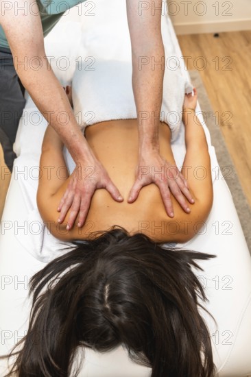 Masseuse performing deep tissue therapy on young womans back, focusing on muscles and shoulders for