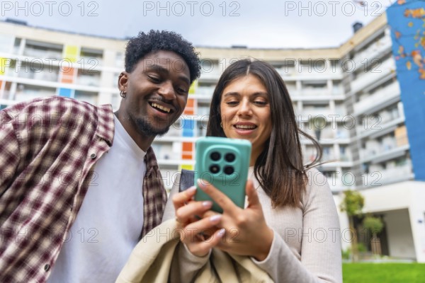 Young diverse friends smiling and sharing content on a smartphone outdoors, enjoying social media,