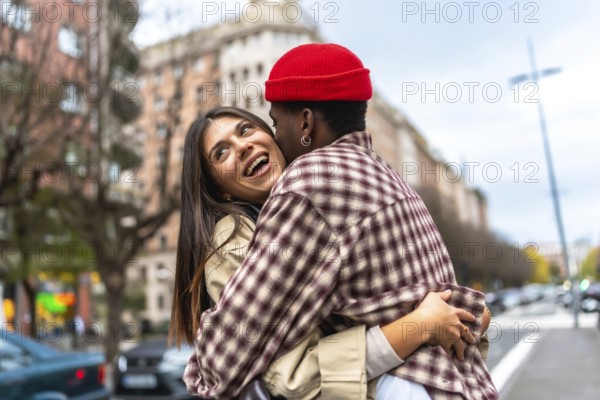 Young diverse couple embracing and laughing together on an urban street, sharing a moment of