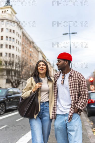 Young interracial couple walking arm in arm on a city street, smiling and talking as they enjoy