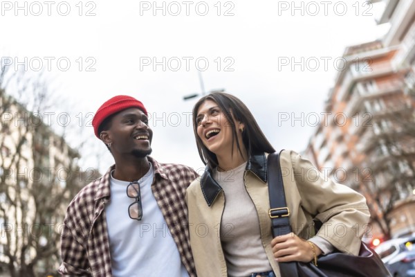 Young diverse couple walking and laughing on a city street, sharing a joyful, candid moment of
