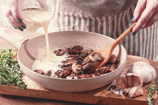 Cooking sauce with mushrooms, a woman pours cream into a pan with mushrooms, natural light,