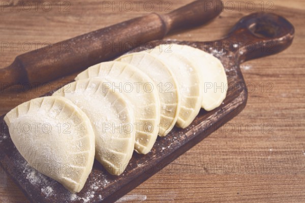 Raw chebureks, mini, on a cutting board, wooden table, close-up, no people
