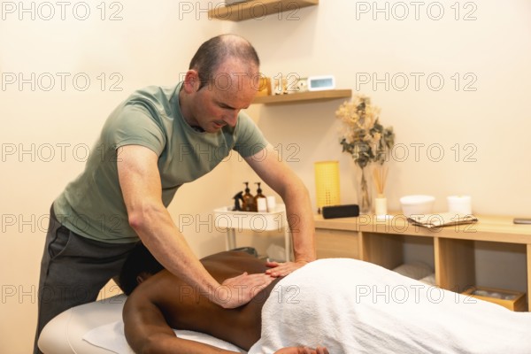 Professional male masseur concentrating while giving a deep tissue back massage to a client lying
