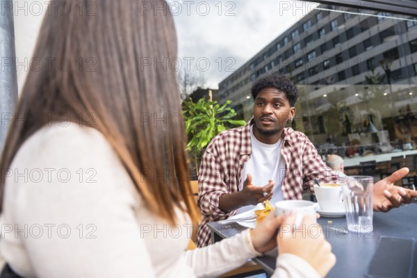 Young man and woman sit at an outdoor cafe in the city, sharing coffee and a serious conversation