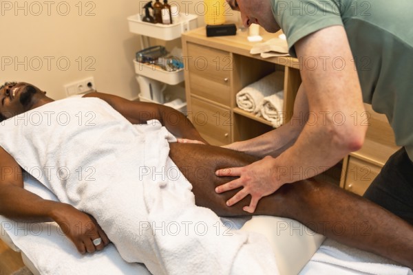African american man lying on a table enjoying a professional leg massage provided by a therapist