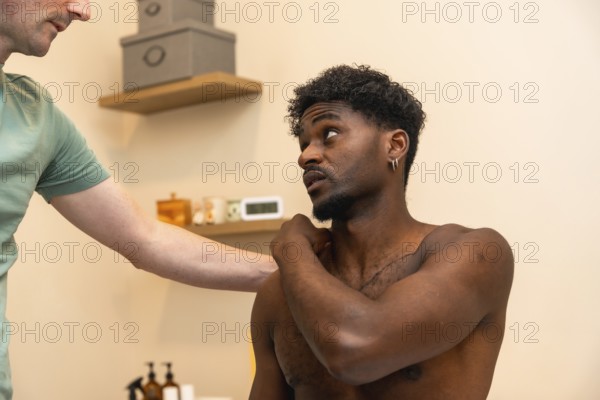 Physiotherapist performing a massage and consulting with a male patient experiencing shoulder pain,