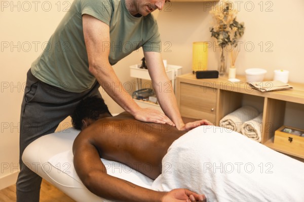 Masseur applying pressure and performing a professional back massage for a male client lying on a