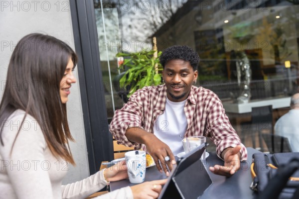 Diverse friends discussing and working together on a modern digital tablet while enjoying coffee at