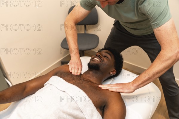 African american man lying on a massage table, smiling and enjoying a professional therapist giving