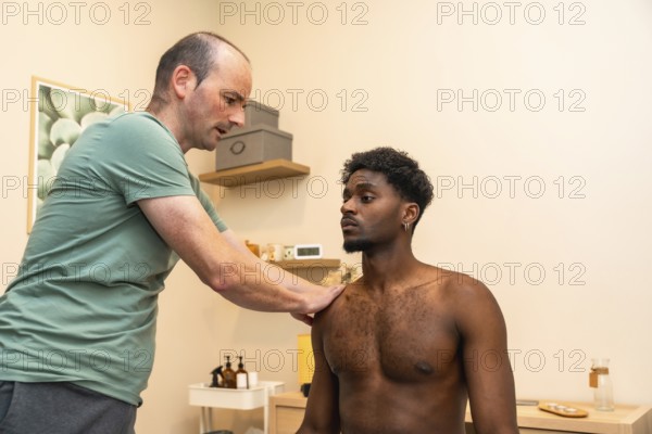 Male practitioner examining a young man's shoulder, providing professional medical care during a