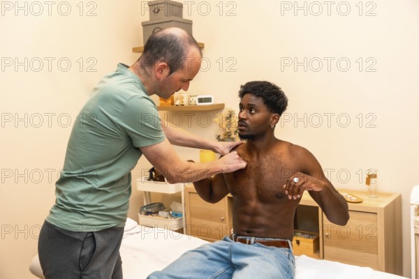 Physical therapist performing an examination and palpation on a young adult male patient's shoulder