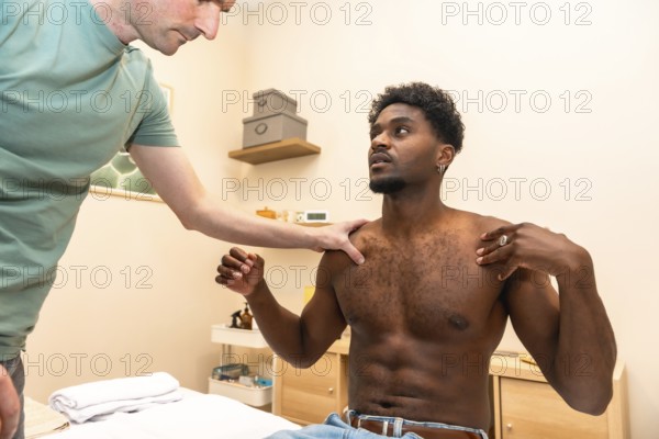 Male physiotherapist examining a young adult patient's shoulder and upper body, assessing mobility